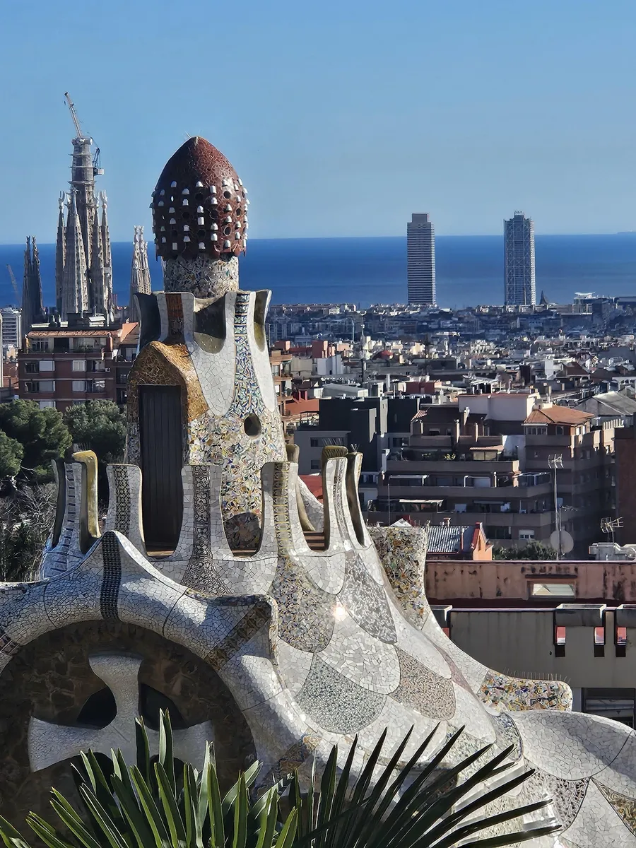Mosaic gatehouse at Park Güell with the Sagrada Família and the sea behind