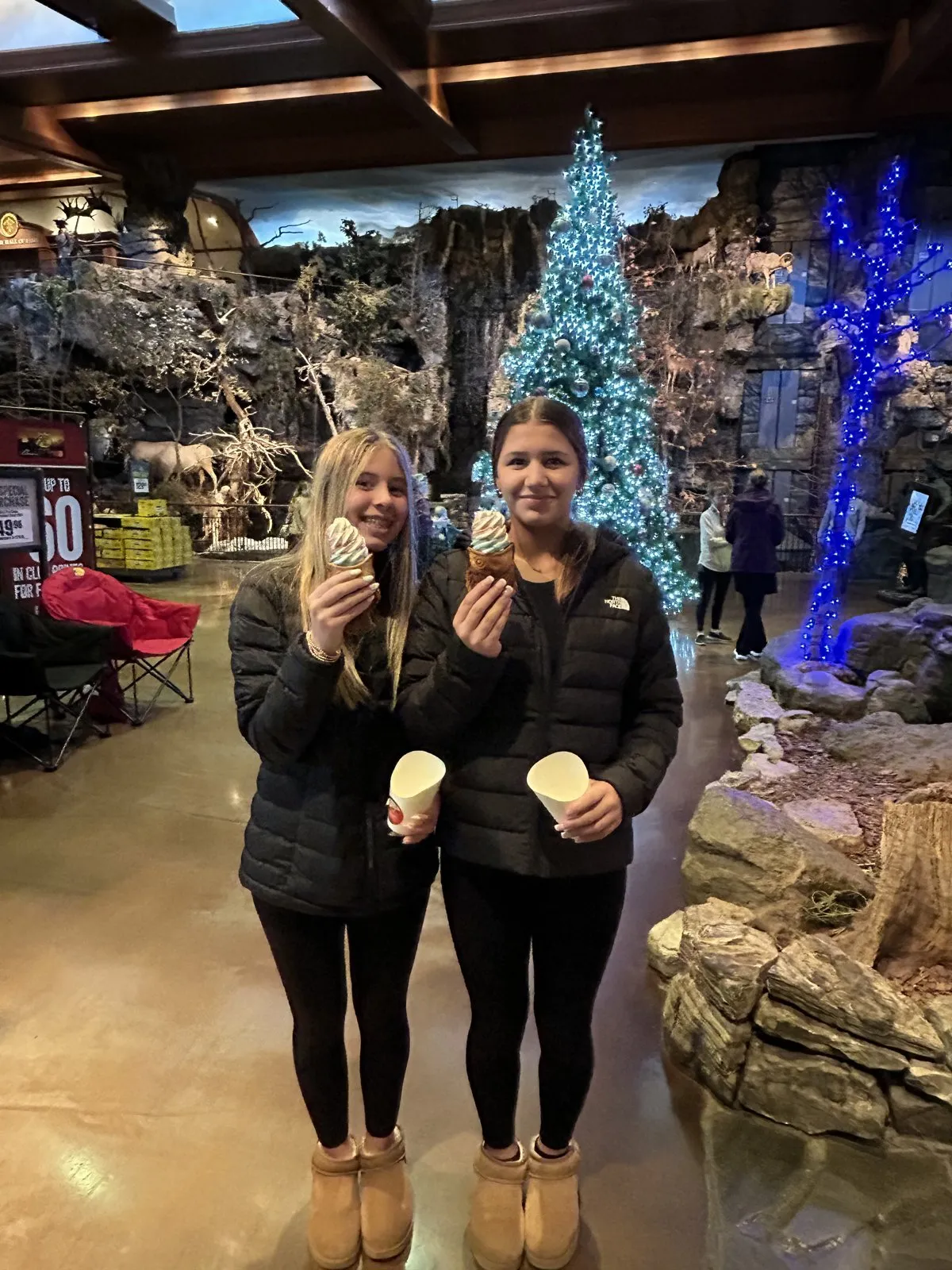 Two girls holding treats inside the Bass Pro Shops flagship with lit Christmas trees behind them