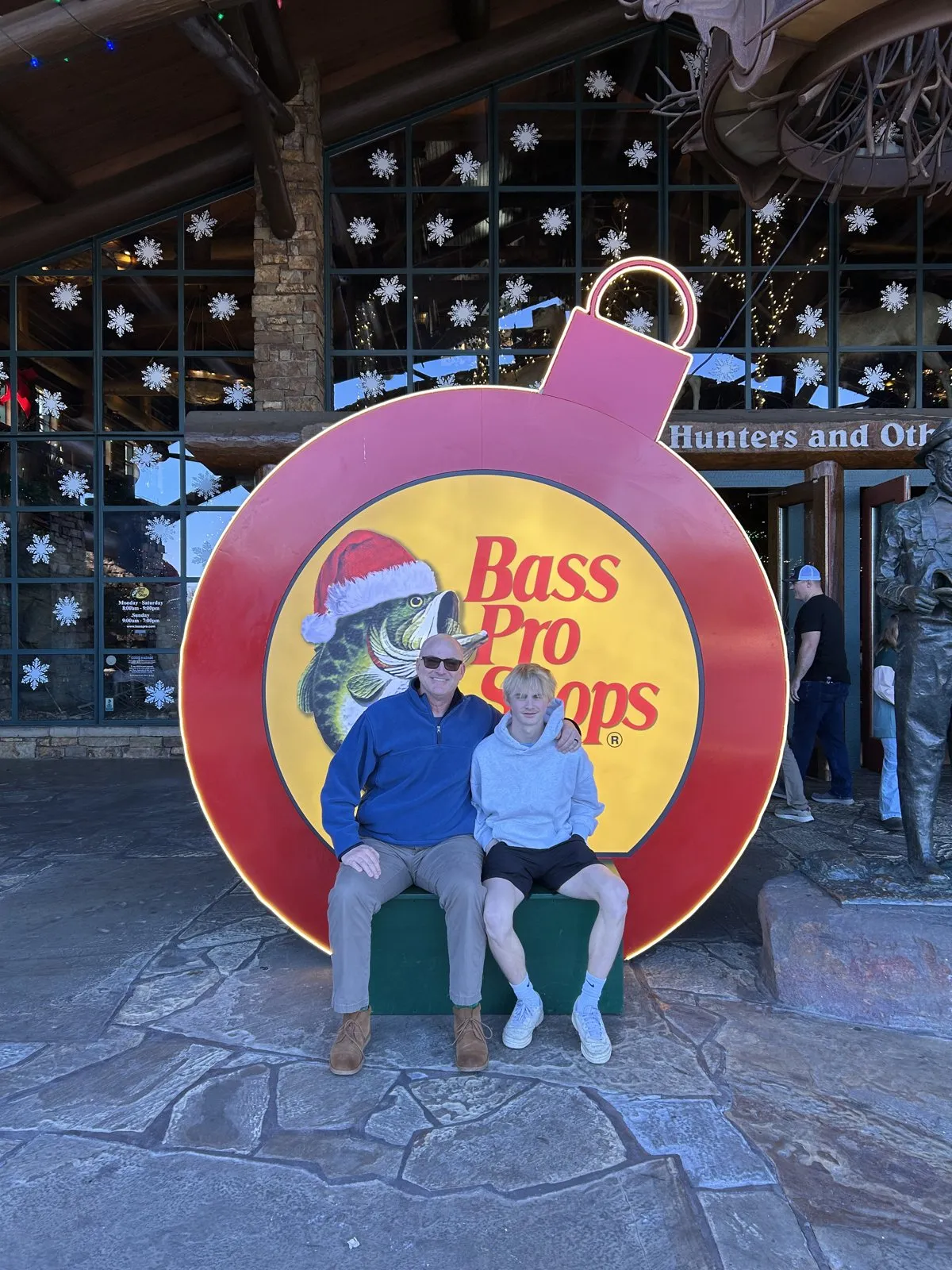 Two of us sitting in front of a giant Bass Pro Shops Christmas ornament