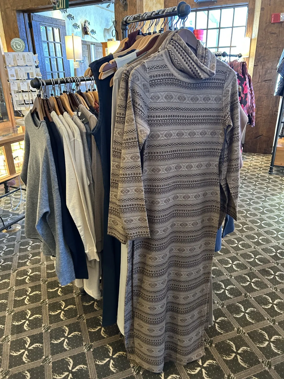 A patterned sweater dress and tops on a rack in the gift shop