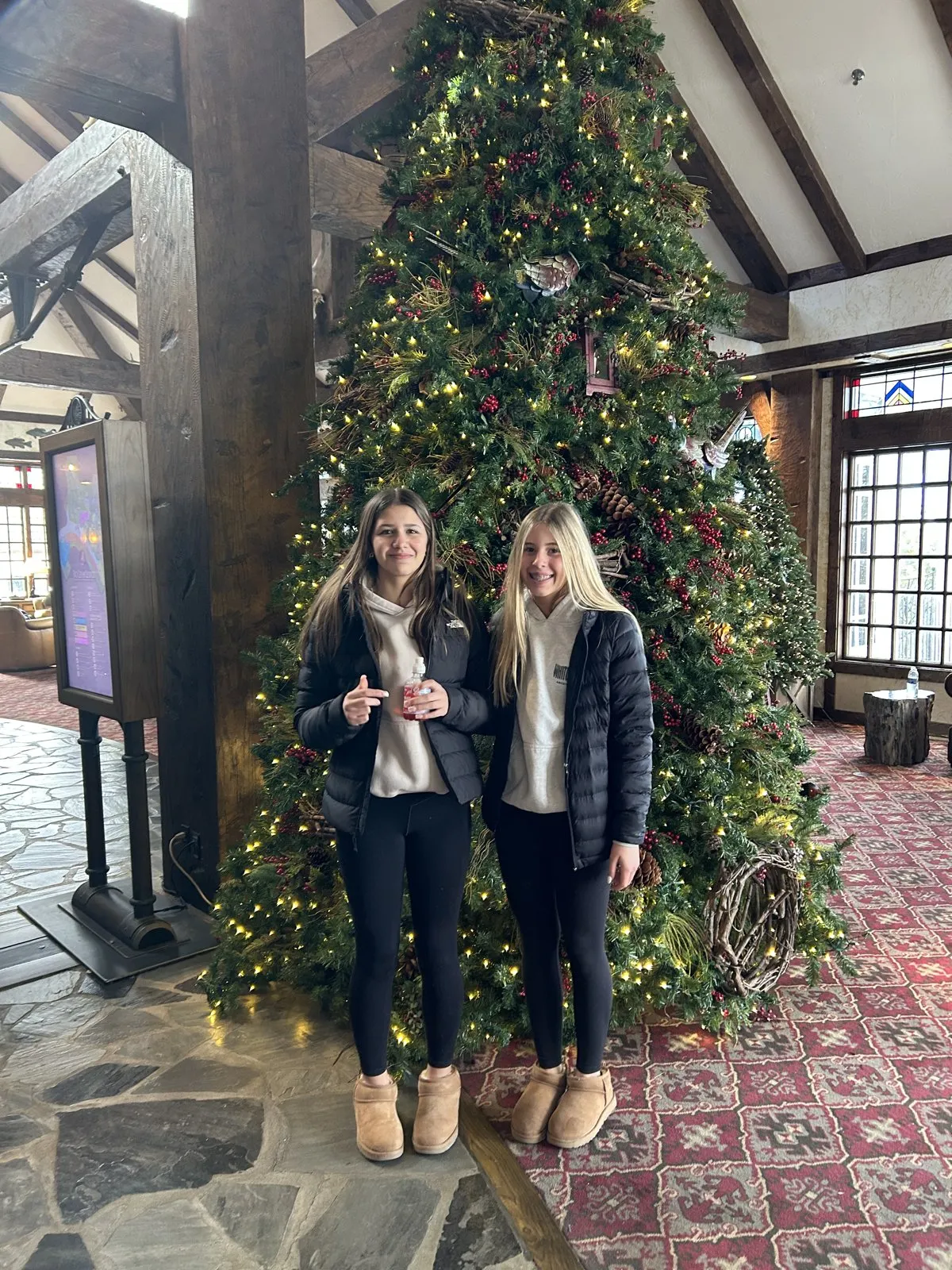 Two girls in front of a tall lit Christmas tree in the timber-beamed lobby at Big Cedar Lodge