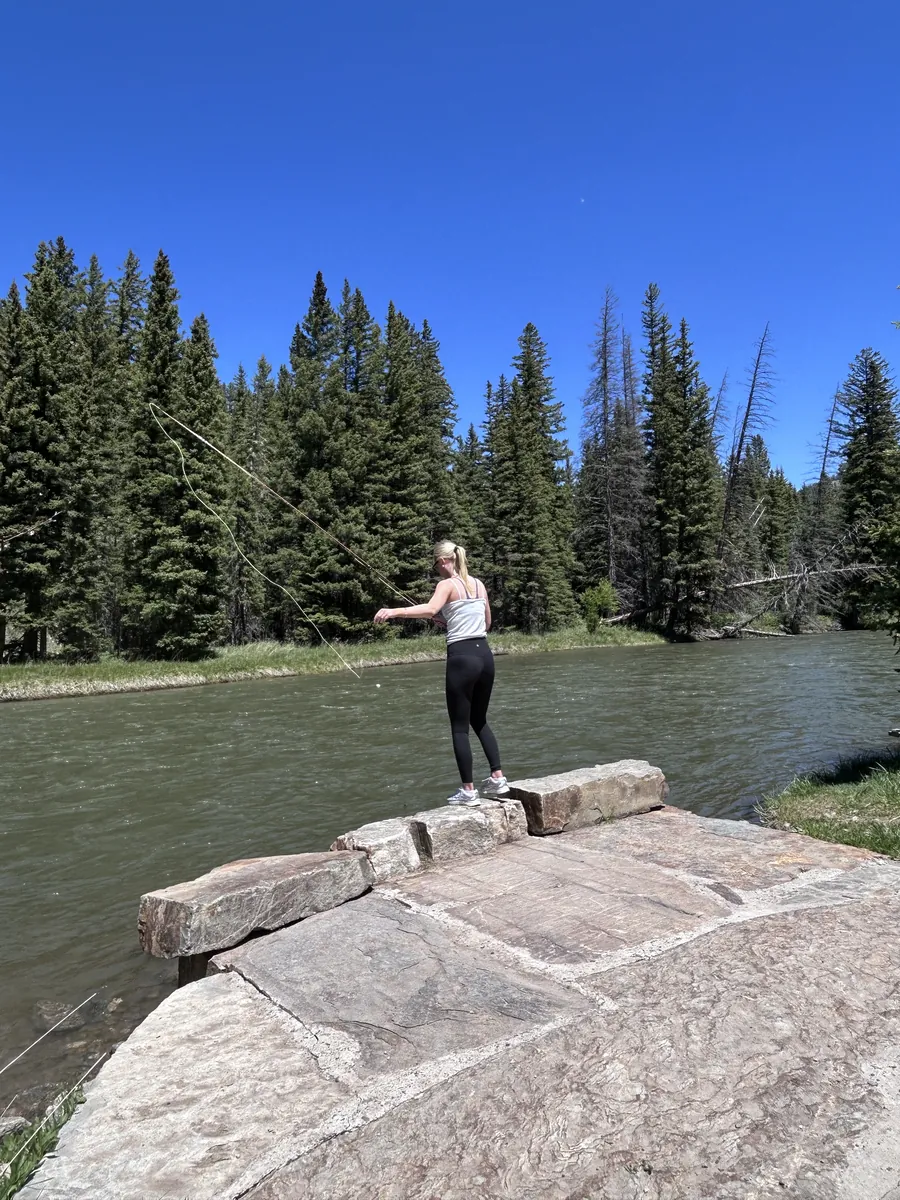 Teen girl fly casting from a stone ledge on the Gallatin River near Big Sky, Montana