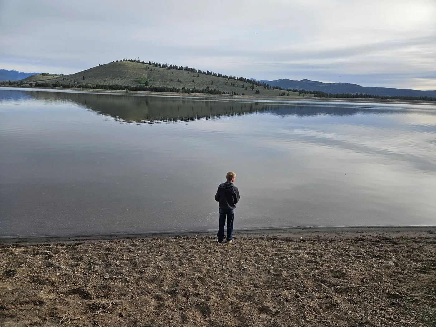 Boy fishing from a sandy shore of a calm lake in the early morning near Big Sky, Montana