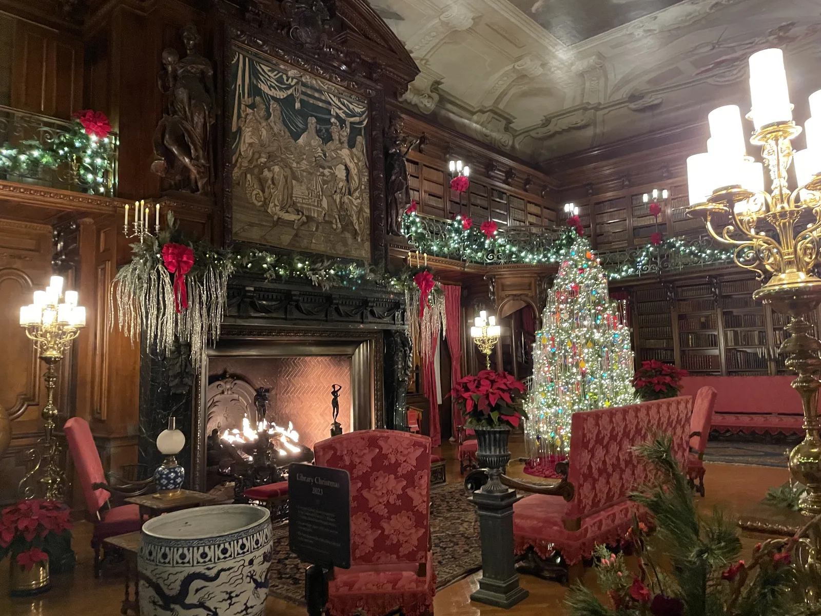 An ornate Biltmore room decorated for Christmas with a lit tree, garland and a roaring fireplace