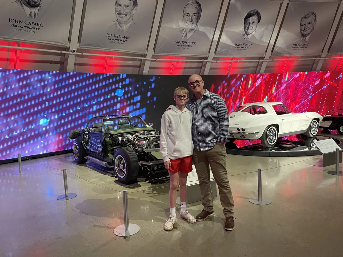 Posing between a Corvette chassis and a classic white Corvette under the designer portrait wall