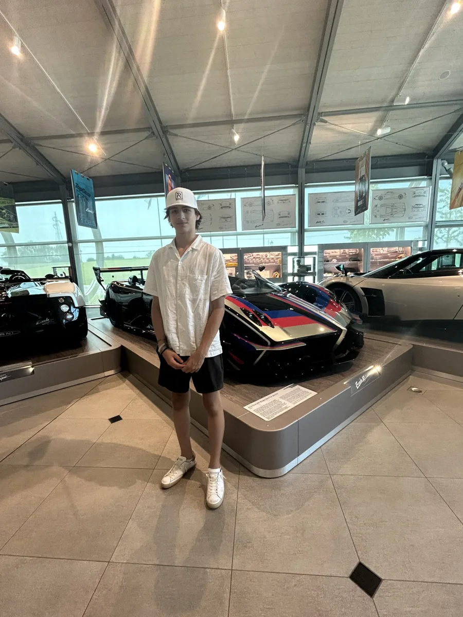 A teen standing beside a Pagani on display at Pagani in Italy