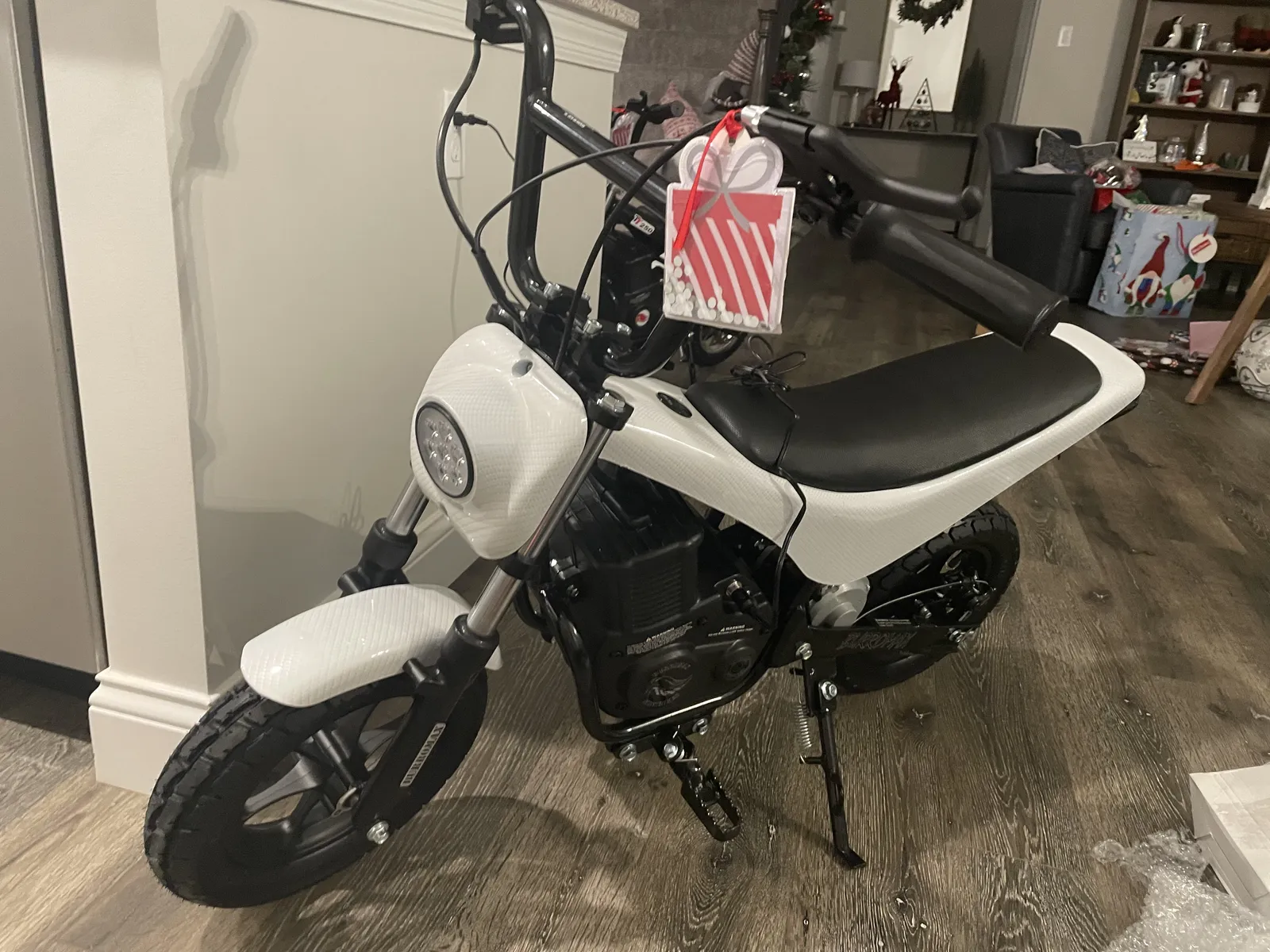 A white electric dirt bike with a gift bow on the handlebars