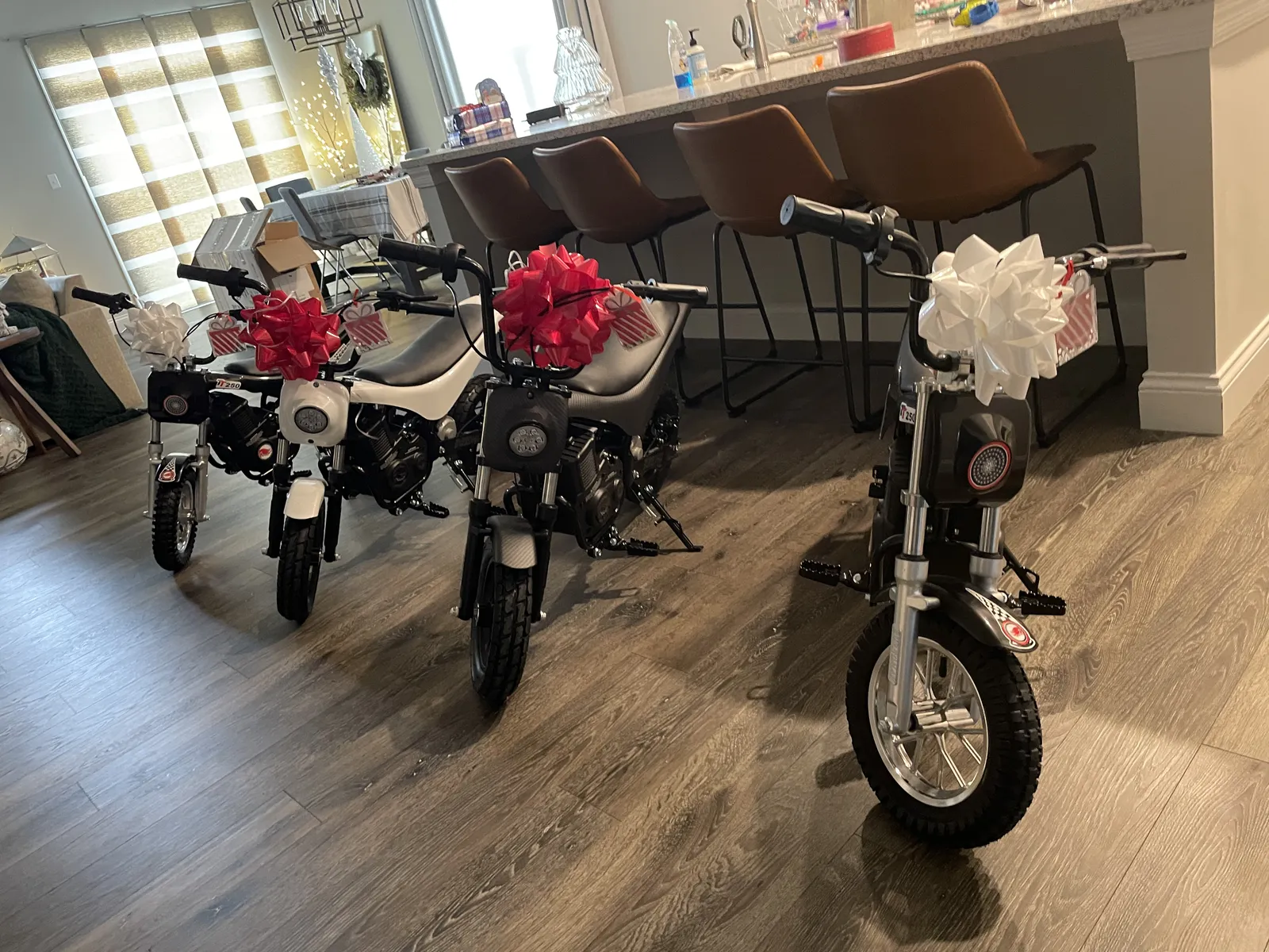 Three electric dirt bikes with red and white bows waiting in the living room on Christmas morning