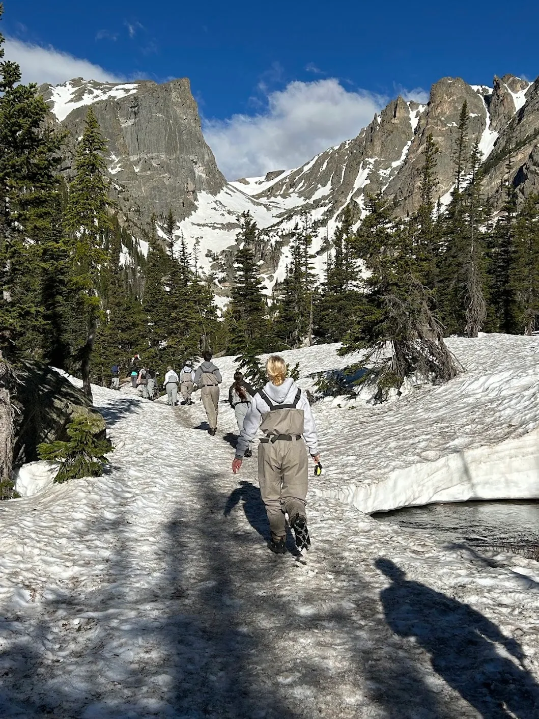 Hiking up through the snow in waders toward Diamond Lake for fly fishing with dramatic Rocky Mountain peaks