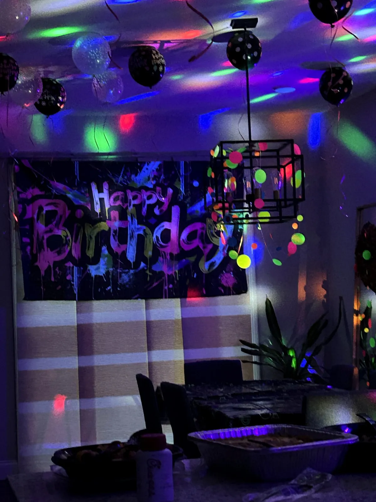 Neon graffiti Happy Birthday banner glowing under blacklight with disco lights on the ceiling