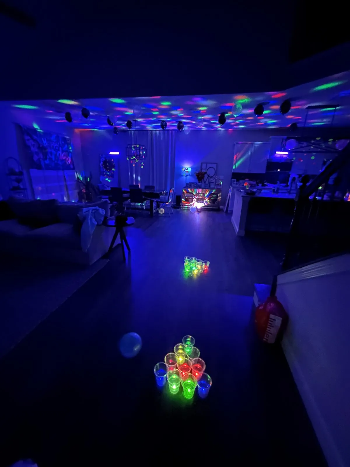 Light-up cup pong game glowing on the floor of a dark room with disco lights on the ceiling