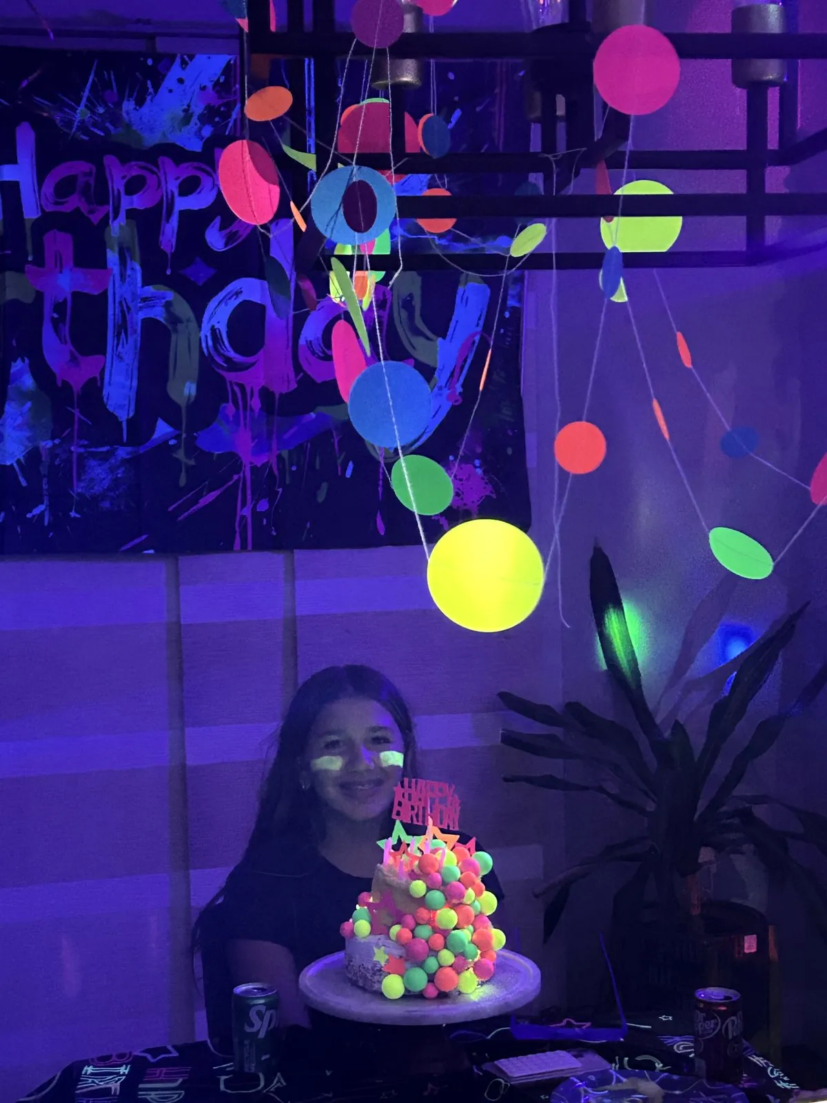 Glowing neon cake on the table under hanging UV dot garland and a graffiti Happy Birthday banner