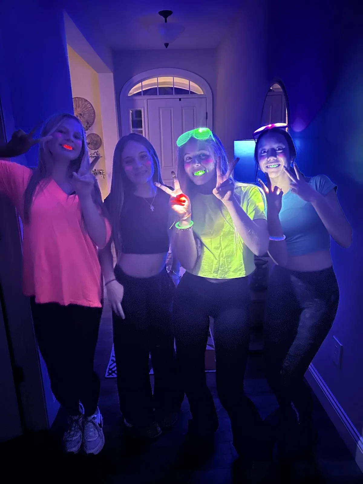 Teen friends in neon shirts with glow stick bracelets posing under blacklight