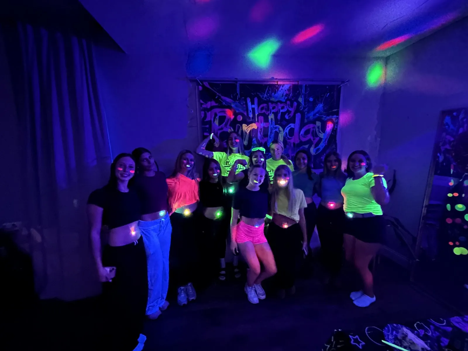 Group of teen girls in neon outfits glowing under blacklight in front of the graffiti birthday banner