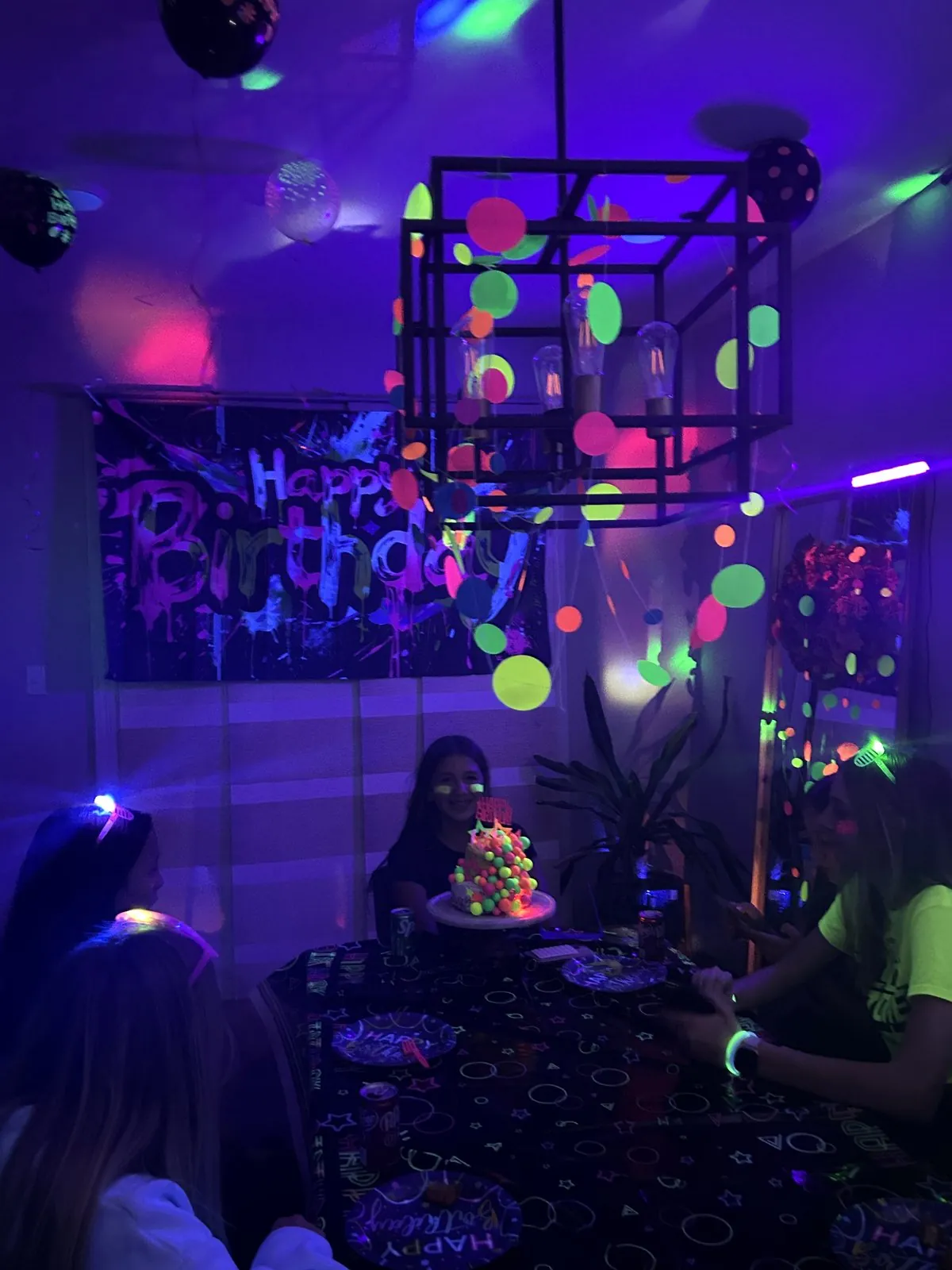 Dinner table under blacklight with dot garland hanging from the light fixture and neon tableware