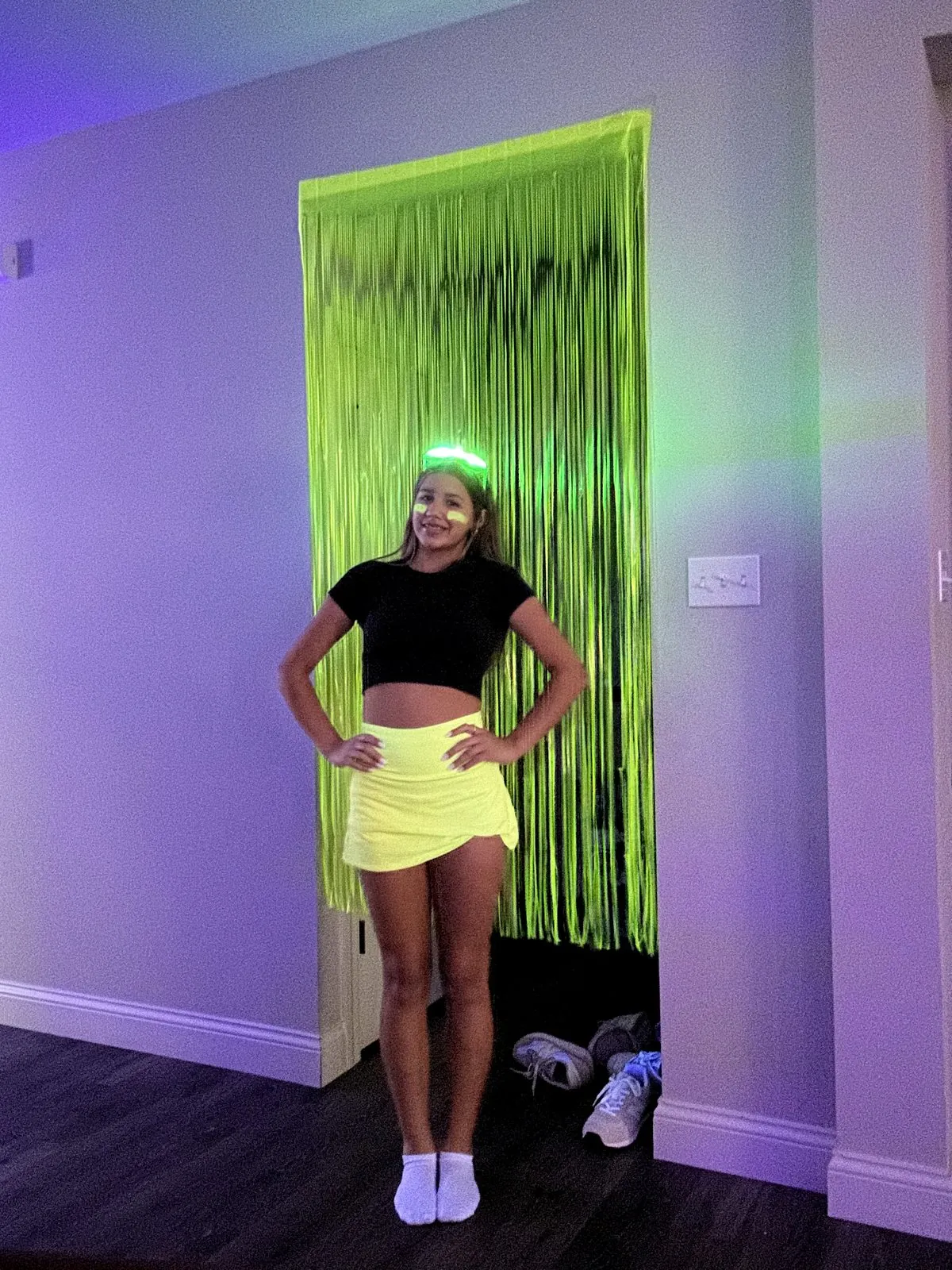 Birthday girl in a neon yellow skirt posing in front of a neon green tinsel curtain