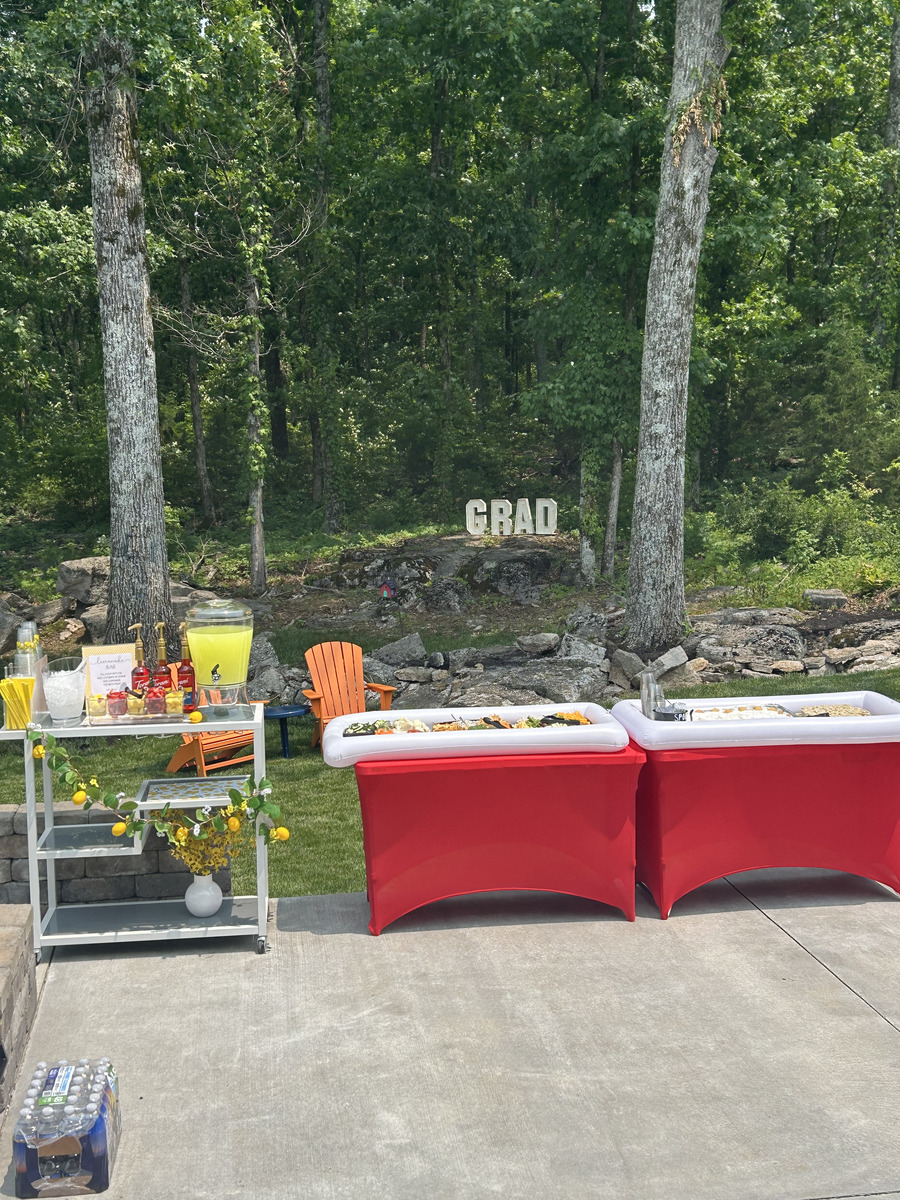 Bar cart set up with a lemonade dispenser, flavored syrups, mason jar cups, and a lemonade bar sign, in front of a GRAD marquee