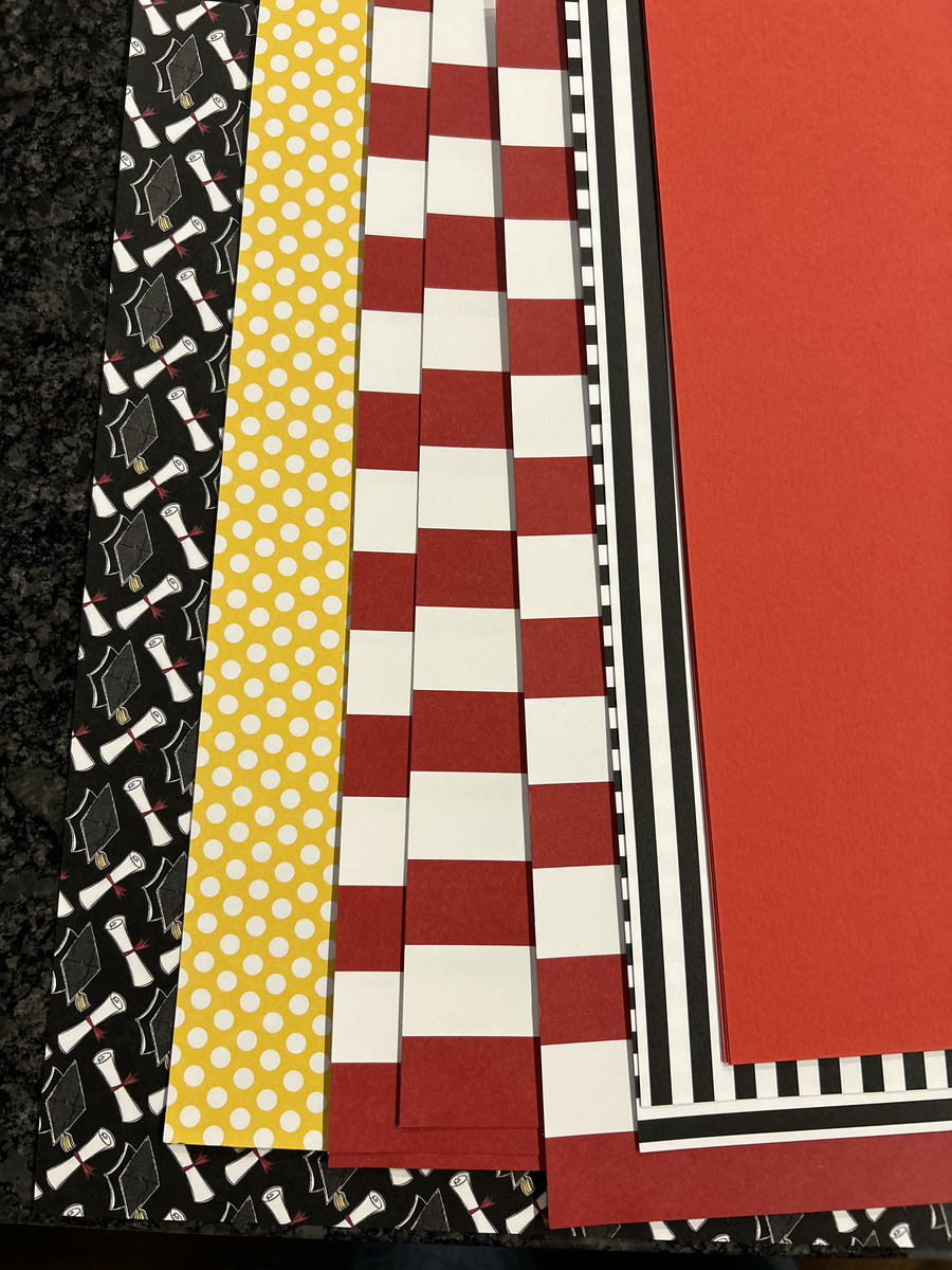 Stack of scrapbook paper in red, black, white, yellow polka dot, stripes, and graduation cap print