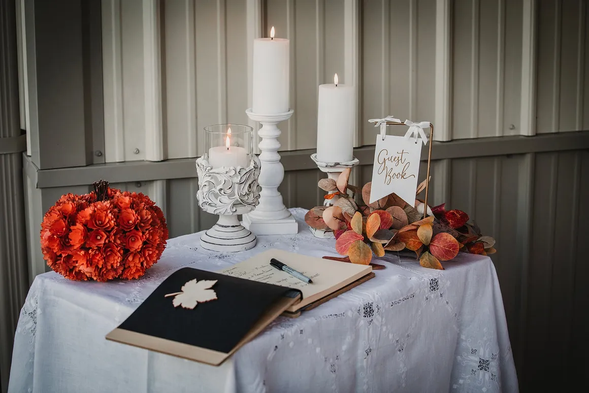Guest book table with white candle holders, fall leaves, and burnt orange floral ball
