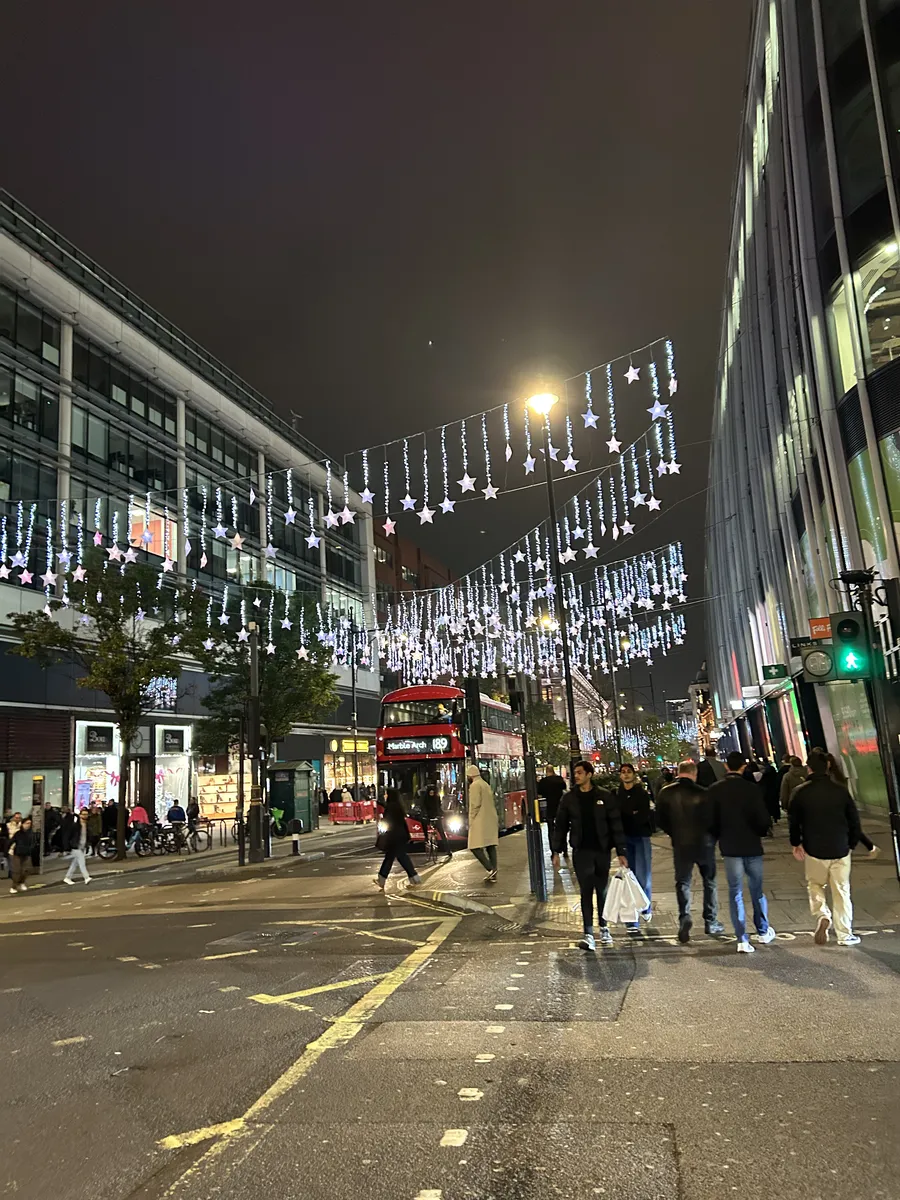 Christmas lights strung over a busy London shopping street at night with a red double-decker bus