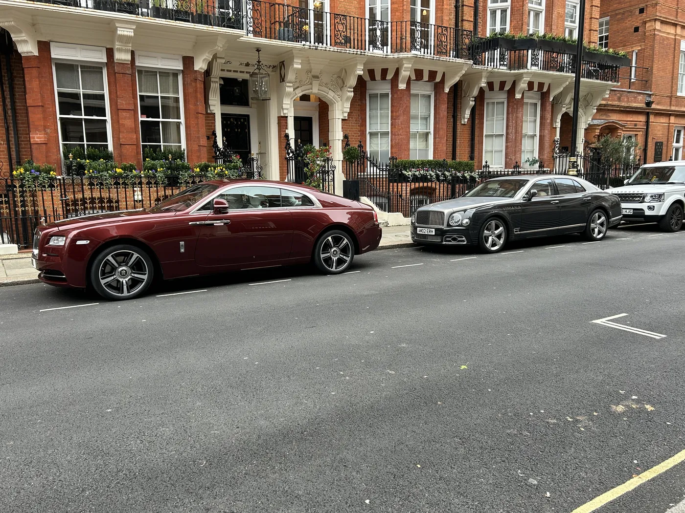 Red-brick Mayfair townhouses with luxury cars parked along the street