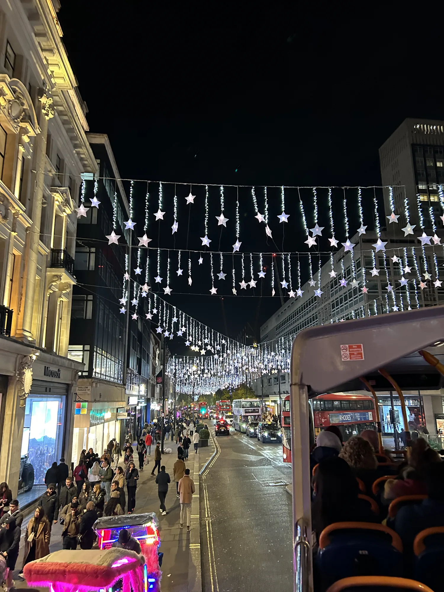 Star-shaped Christmas lights over a London street, seen from the top of a red bus tour