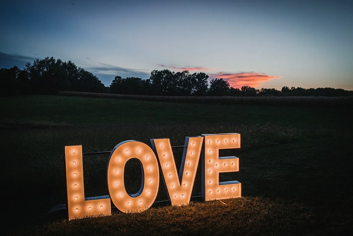 LOVE marquee sign glowing at dusk in the field with a pink and purple sunset behind it
