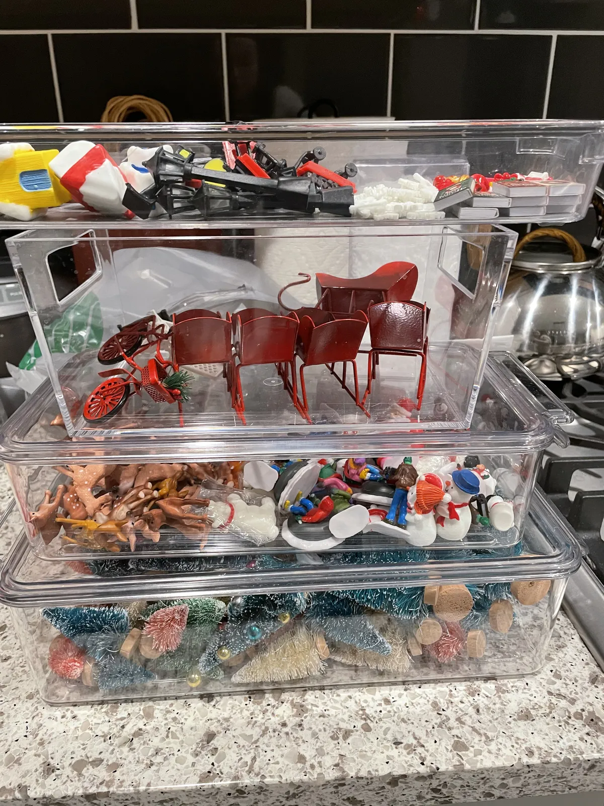 Stacked clear bins filled with tiny trees, figures and Christmas decorations for snow globes