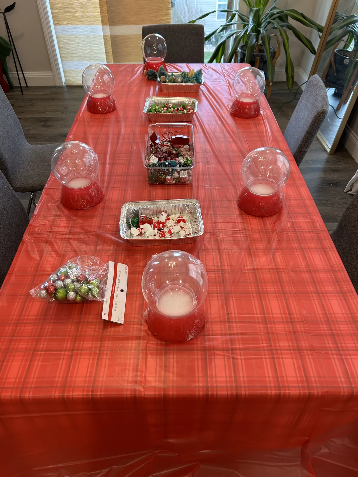 A long table with a red tablecloth, empty glass snow globes at each seat and bowls of supplies