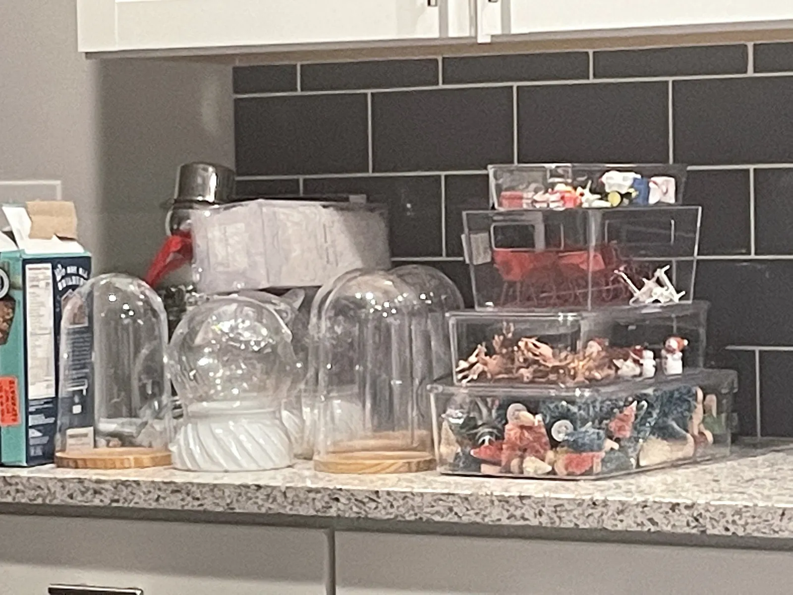 Empty glass snow globes and bins of miniature Christmas figures on a kitchen counter
