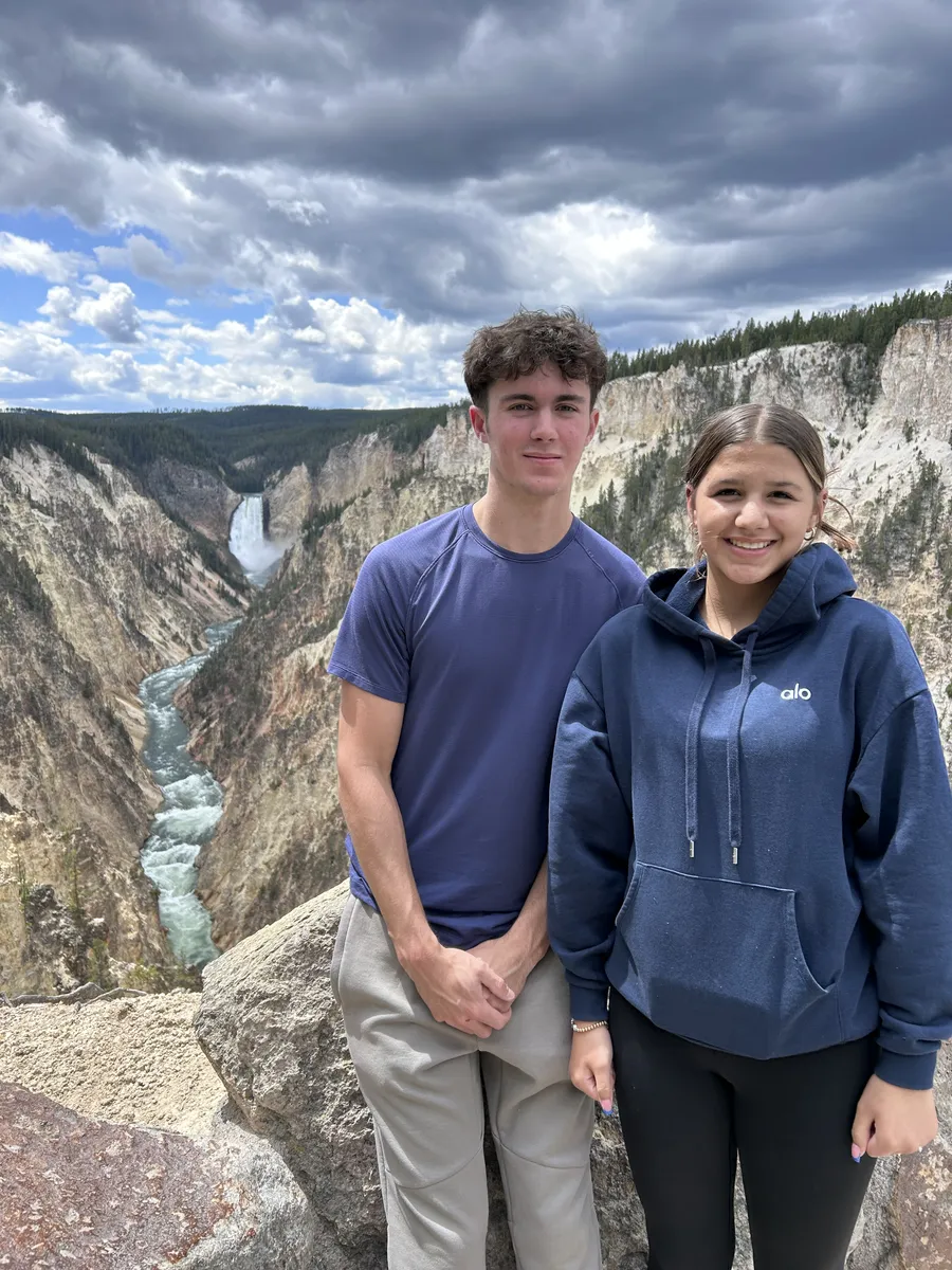 Two teenagers posing above the Grand Canyon of the Yellowstone with the Lower Falls behind them