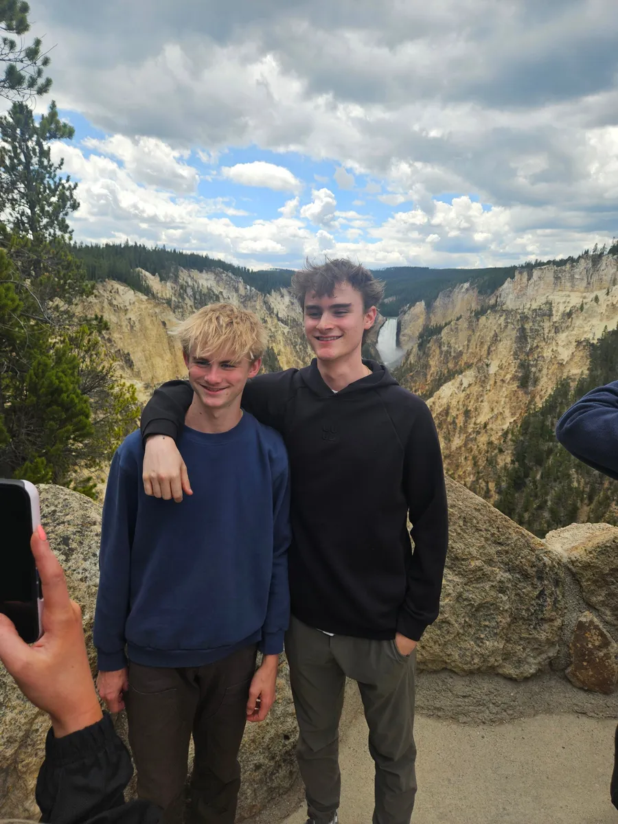 Two teenage boys posing above the Grand Canyon of the Yellowstone with the Lower Falls behind them