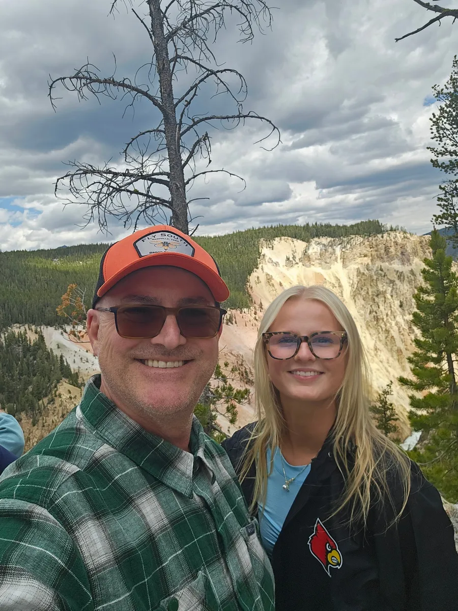 Jason and his daughter taking a selfie above the yellow walls of the Grand Canyon of the Yellowstone