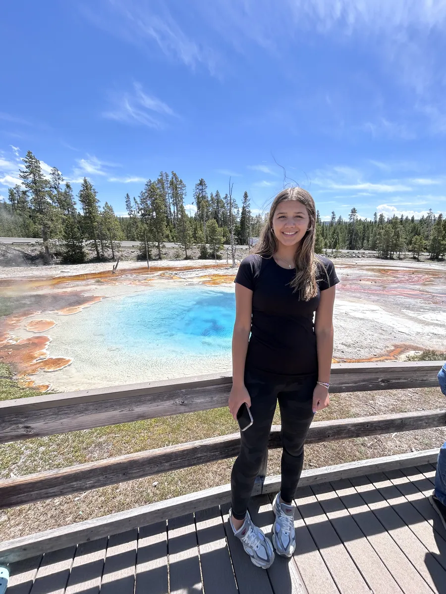 Teen girl on the boardwalk at Midway Geyser Basin with blue hot spring behind her